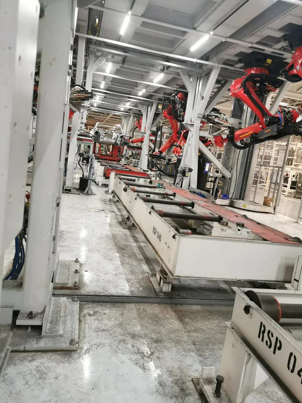 Sistema de conveyor transportando estructura automotriz junto a brazos robóticos